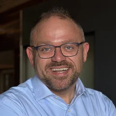 Noah Kaye smiling, in glasses and a light blue shirt